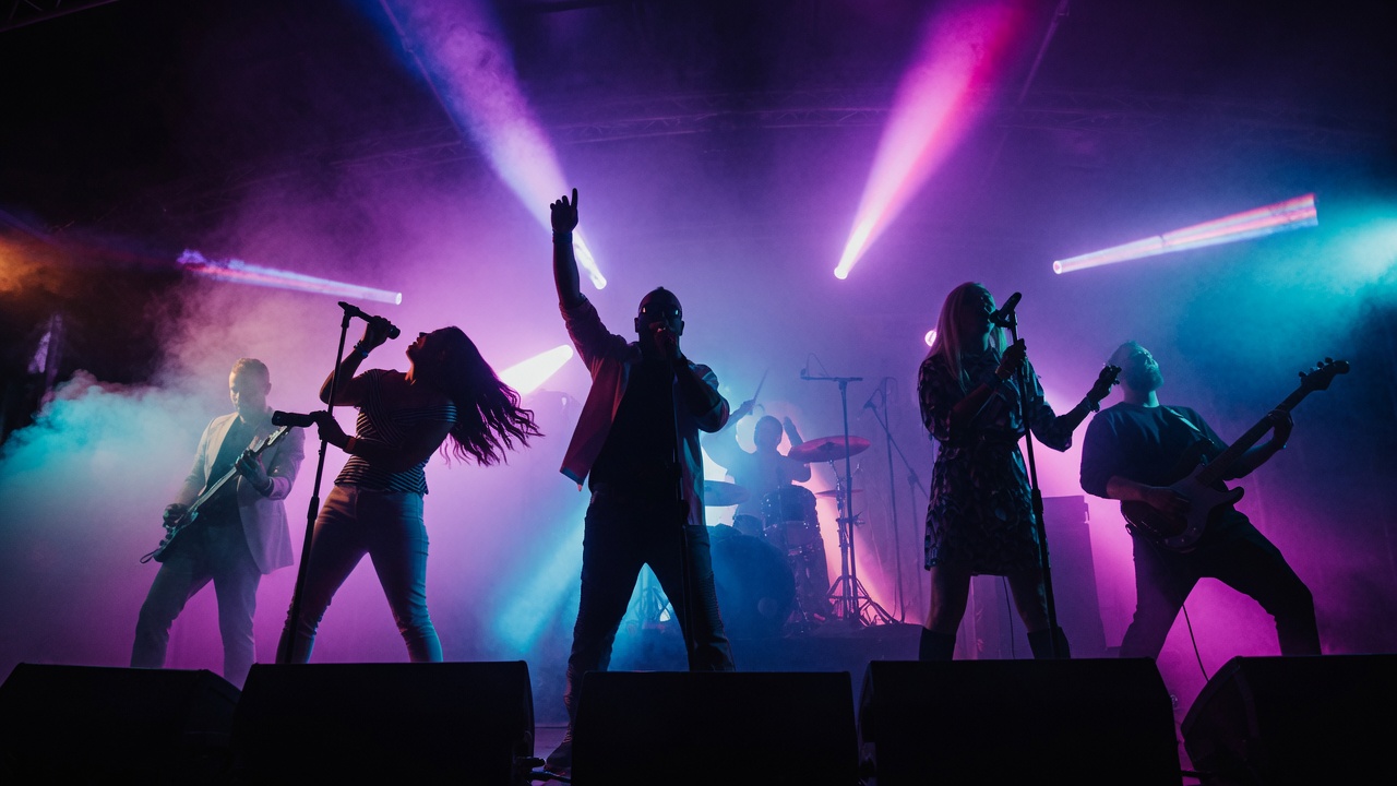 Danger80s live — the 6-piece 80s tribute band on stage under neon lights, frontman centre with the two lead vocalists either side